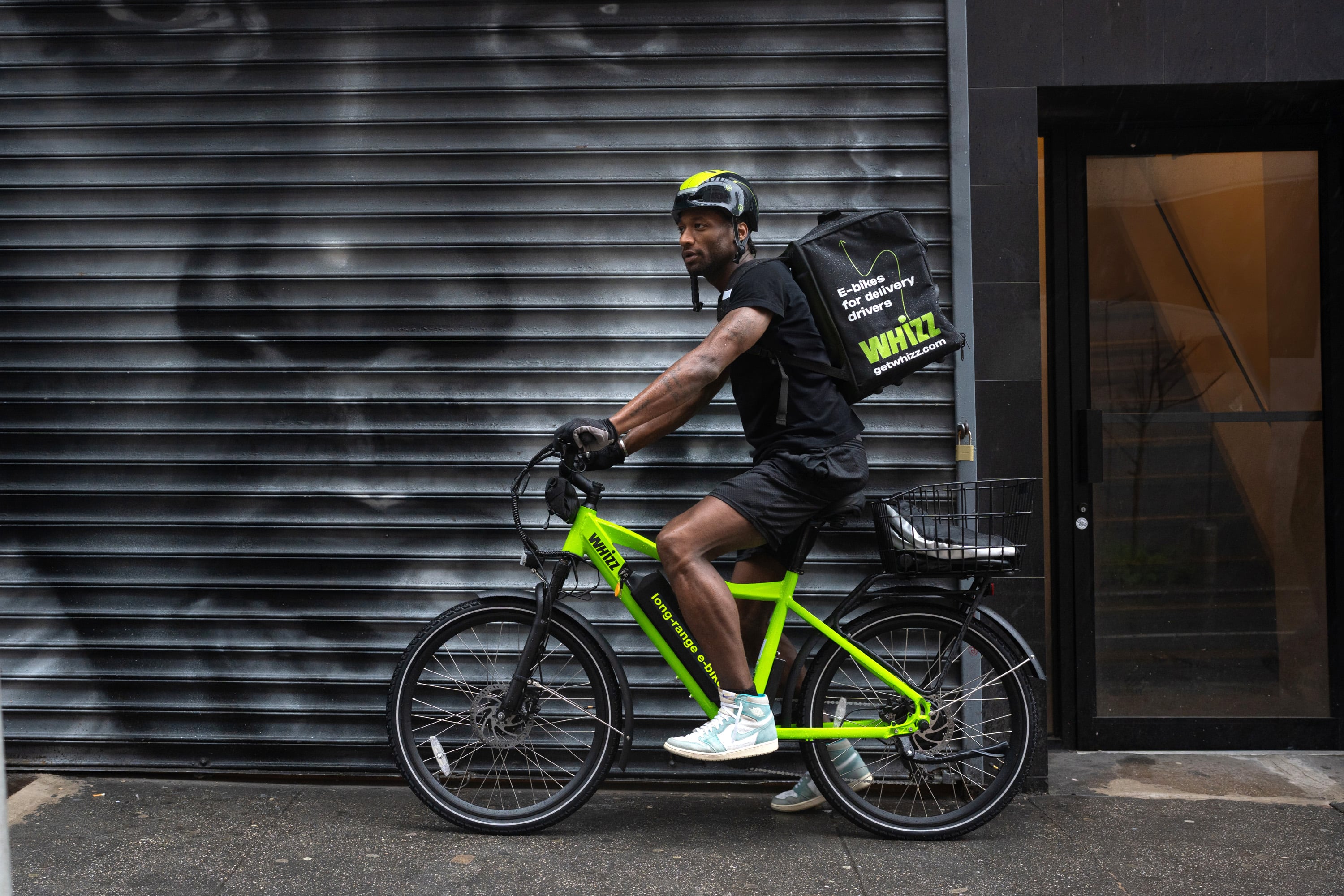 A courier riding a green Whizz e-bike past a New York street mural