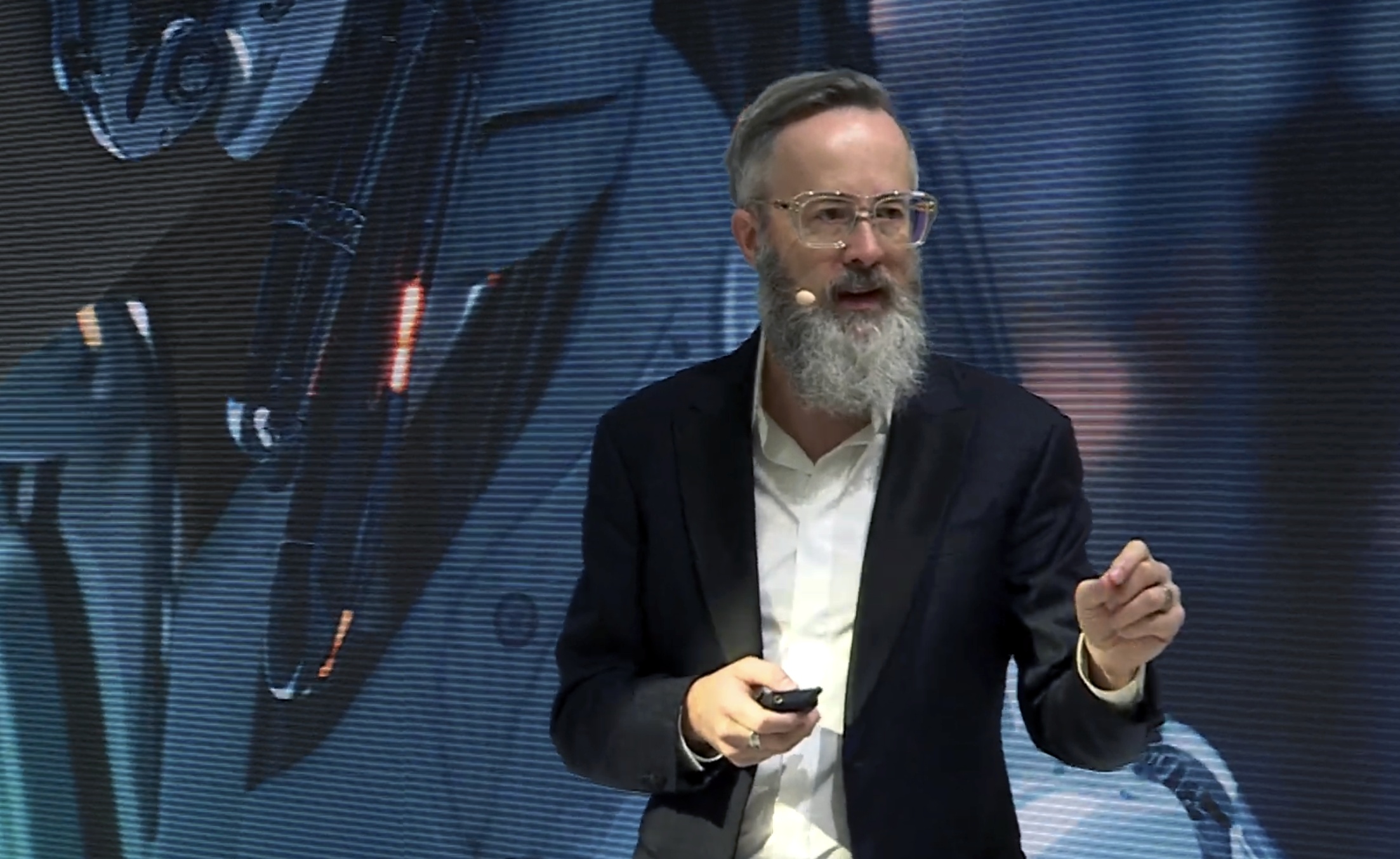 whurley speaking on a conference stage, holding a presentation remote