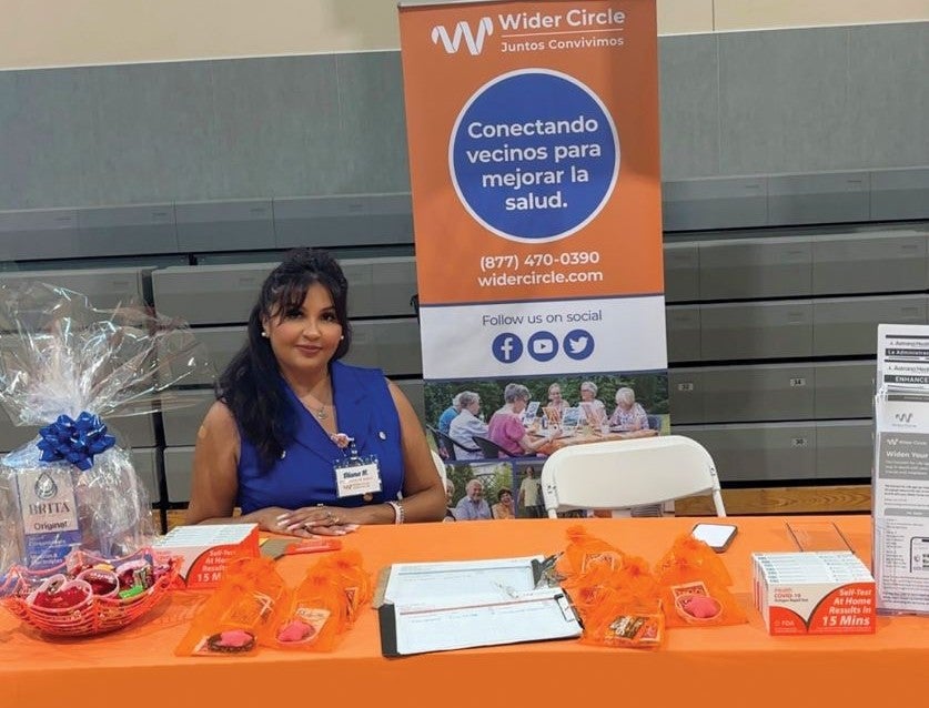 A Wider Circle representative at a community outreach table with Spanish-language Wider Circle signage