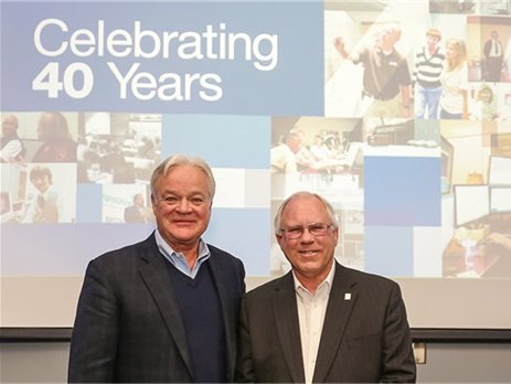 Ron Fauquher and Wil Davis standing together in front of an Ontario Systems anniversary display