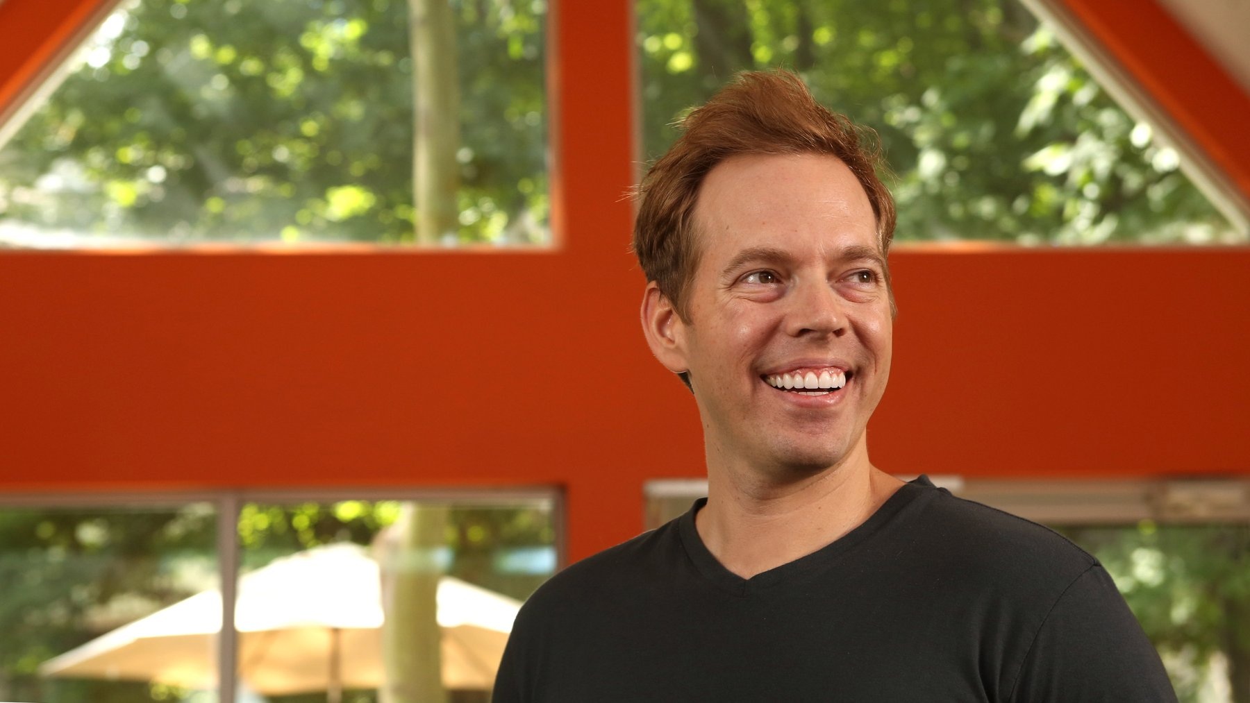 Wil Schroter smiling in a bright interior framed by orange beams