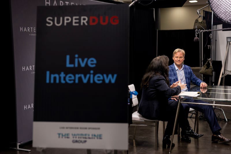 Wil VanLoh, seated at right in a blue checked jacket, being interviewed by Deon Daugherty at SUPER DUG 2026