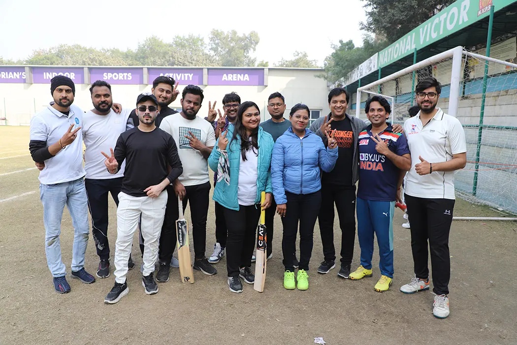 Wildnet colleagues posing together outdoors with cricket bats beside a football goal