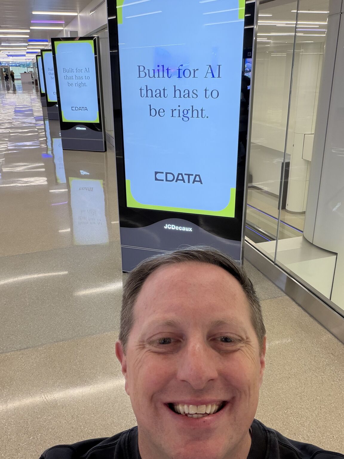 Will Davis smiling in front of CData advertising screens at Orlando International Airport