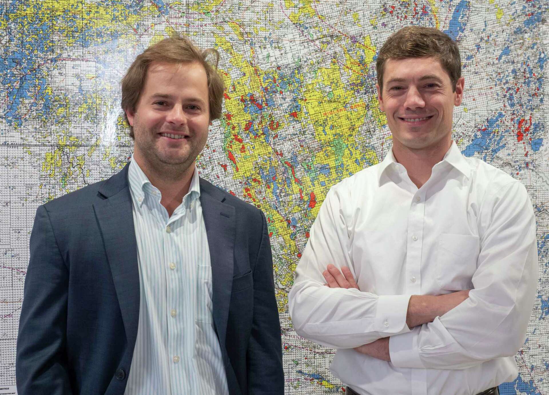 Will Hickey, left, and James Walter standing in front of a detailed Permian Basin acreage map