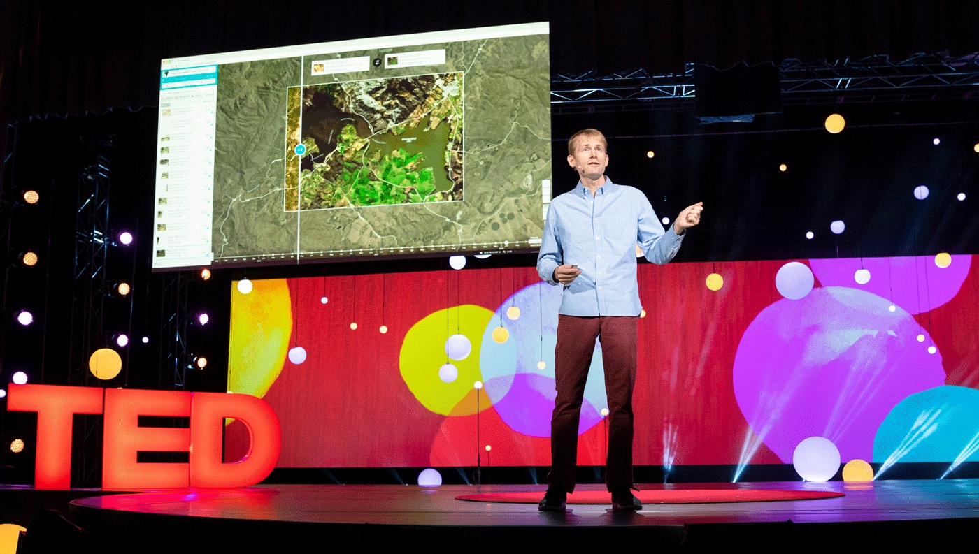 Will Marshall speaking at TED2018 beside a large display of satellite imagery