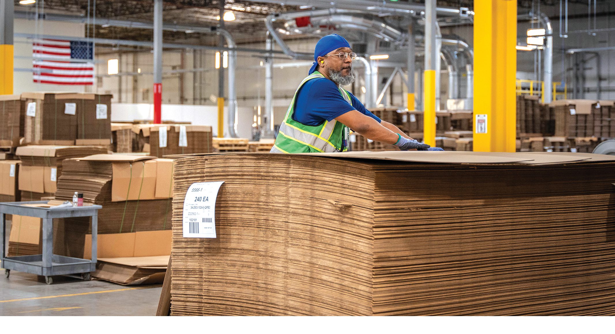 A worker handling sheets of corrugated packaging inside a UFP manufacturing facility