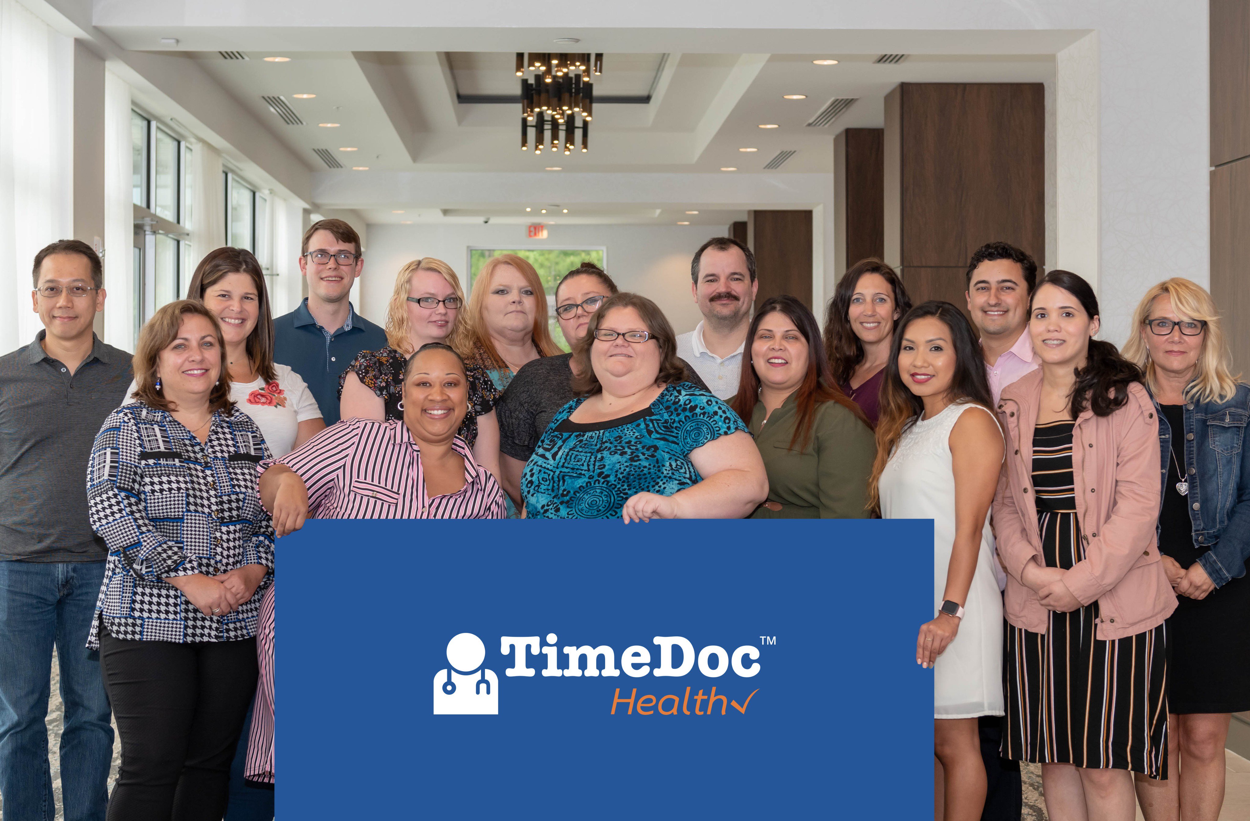 TimeDoc colleagues gathered behind a blue company sign in a bright room