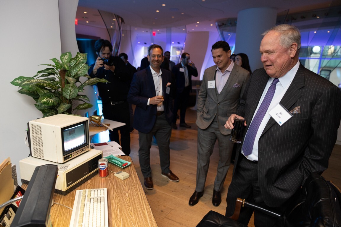 Bill Stone standing beside vintage desktop computers at an SS&C anniversary gathering