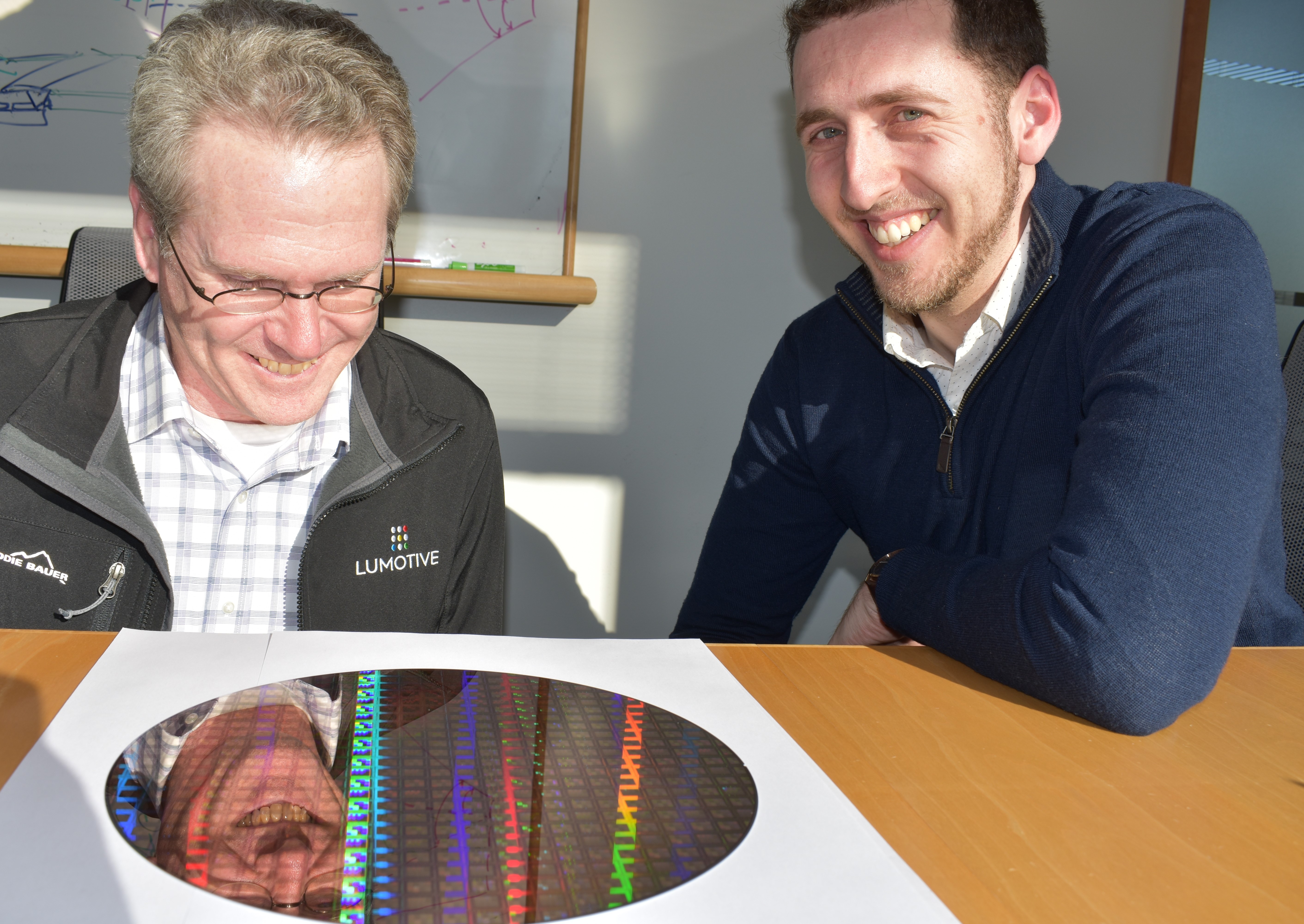 William Colleran, left, and Gleb Akselrod smiling beside a patterned semiconductor wafer at Lumotive