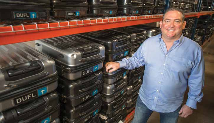 Bill Rinehart beside orange warehouse shelves stacked with DUFL suitcases