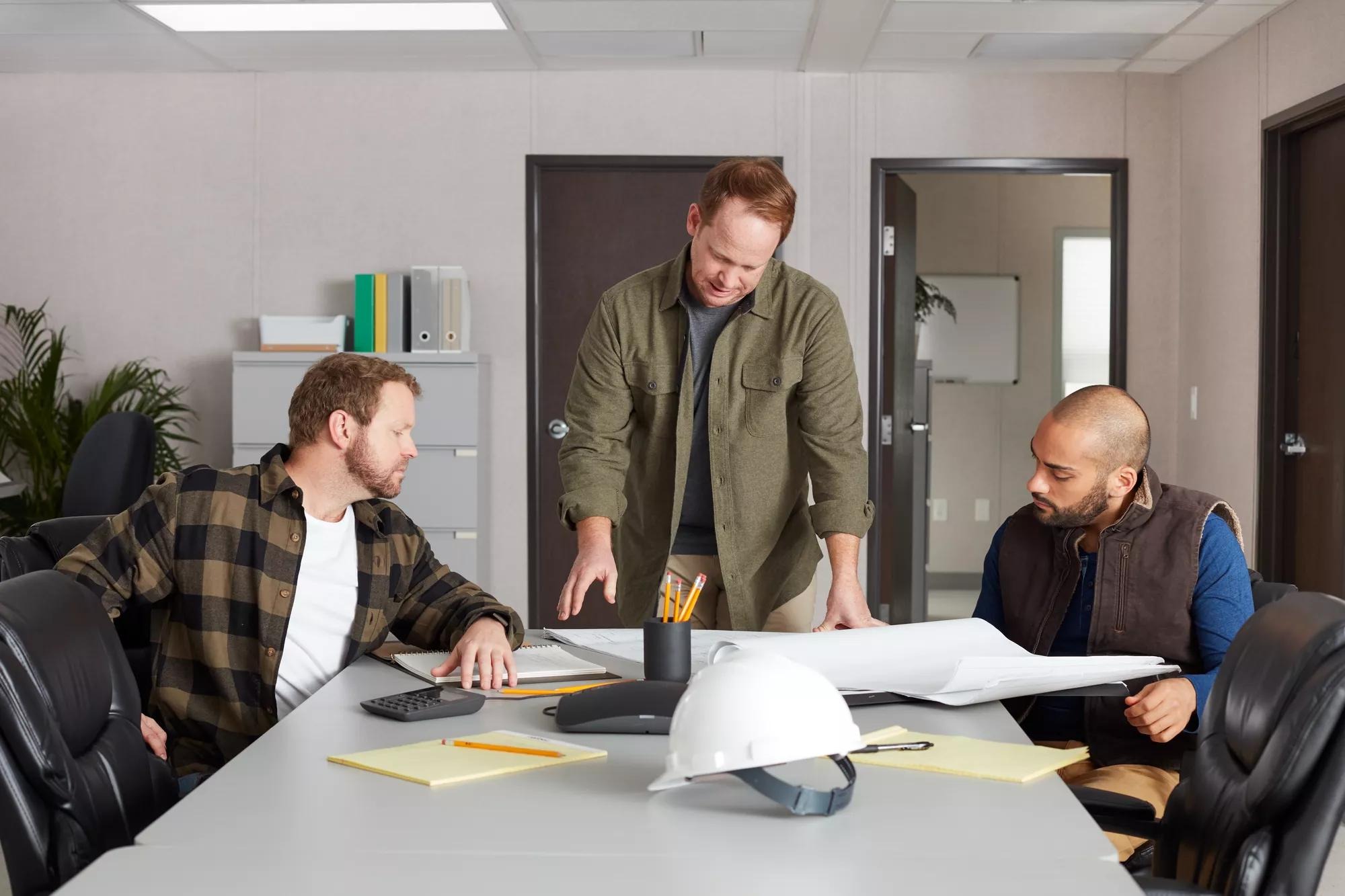 Construction professionals reviewing plans around a table inside a furnished temporary workspace