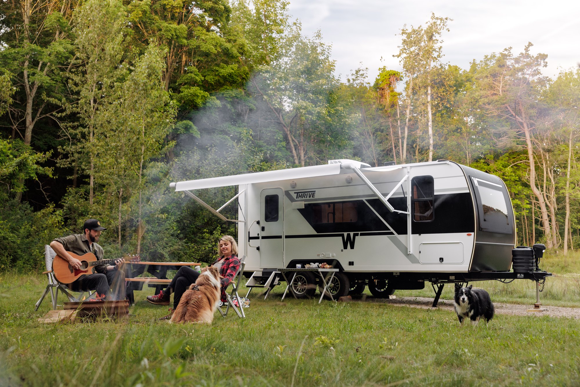 A Winnebago Thrive travel trailer at a campsite with an awning open