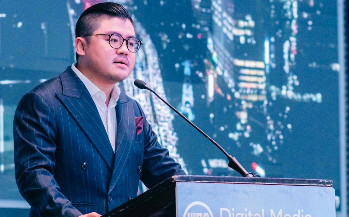 Winston Utomo in a pinstripe suit speaking at a lectern at Digital Media Asia