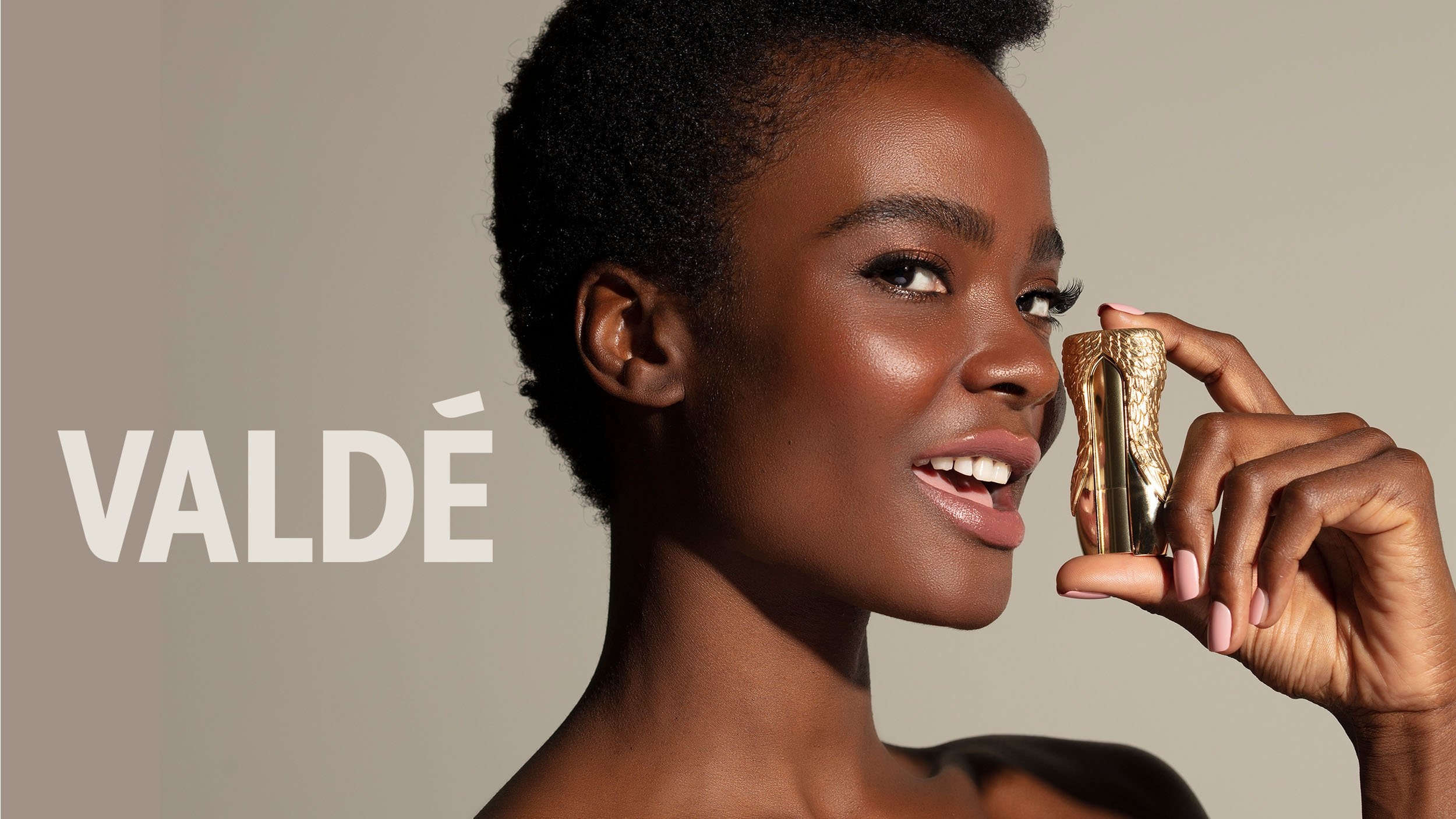 Valdé campaign image showing a model holding a sculptural gold-colored lipstick case