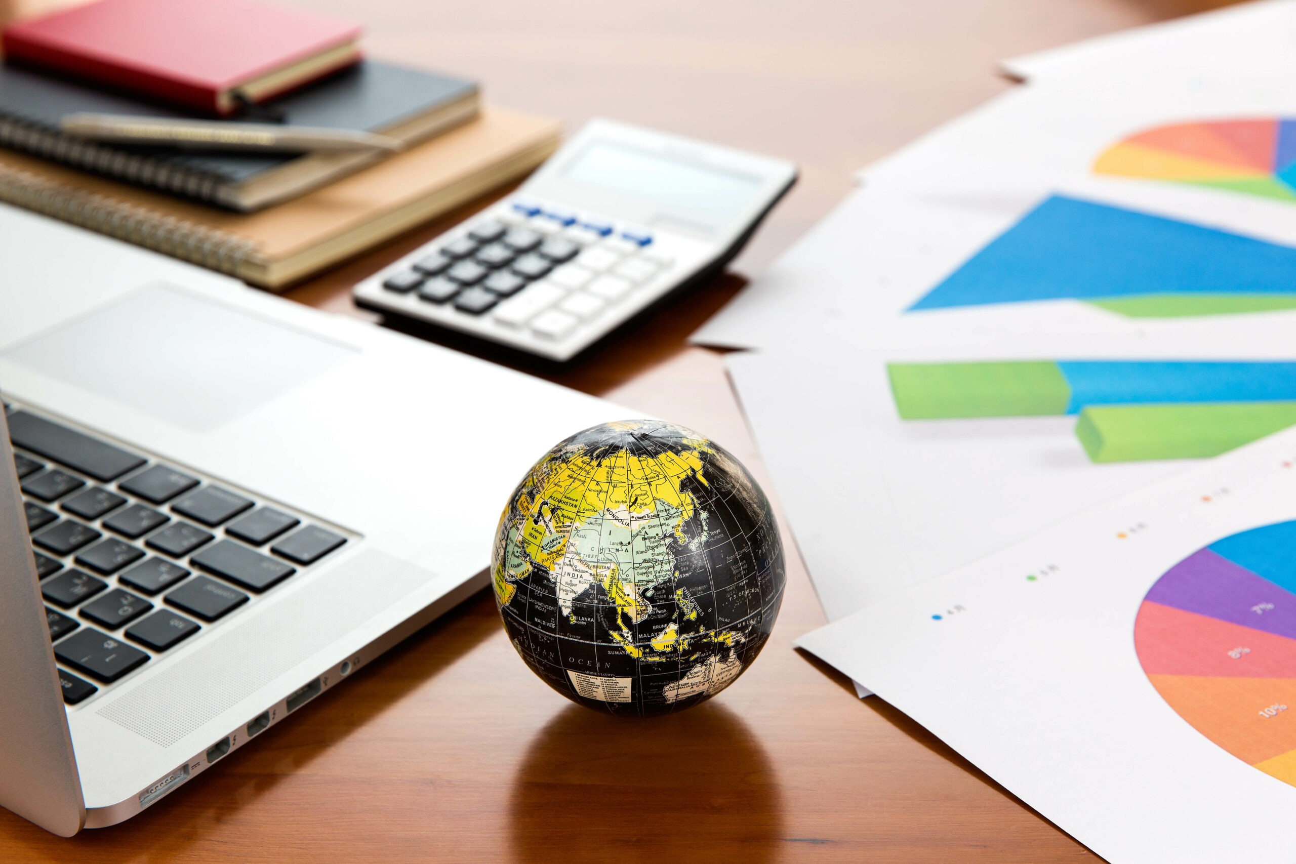 A desk with a globe, laptop, calculator and printed financial charts