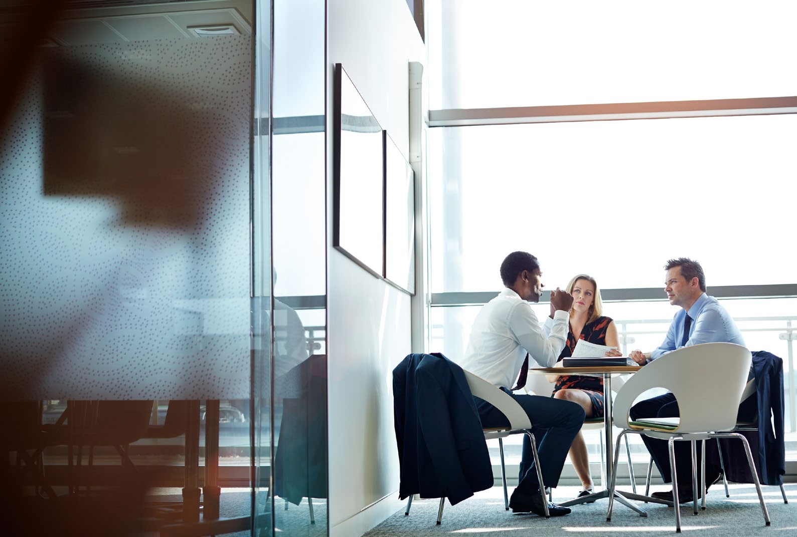 Three people discussing paperwork around a small table in a bright office