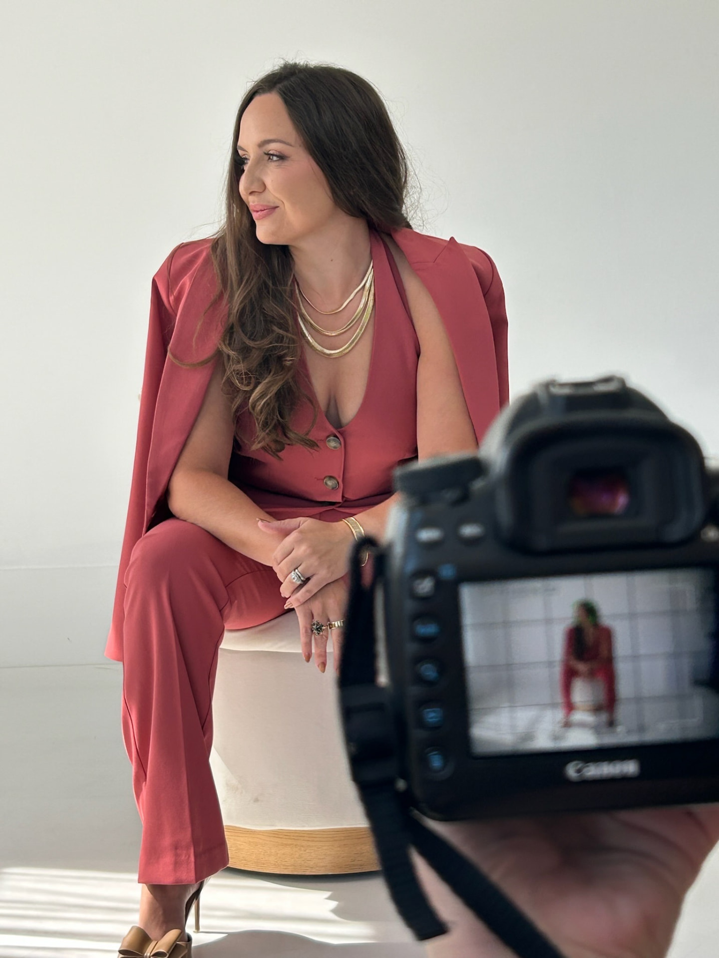 Melissa Barker seated in a red suit during an art-directed brand photoshoot, with a camera in the foreground
