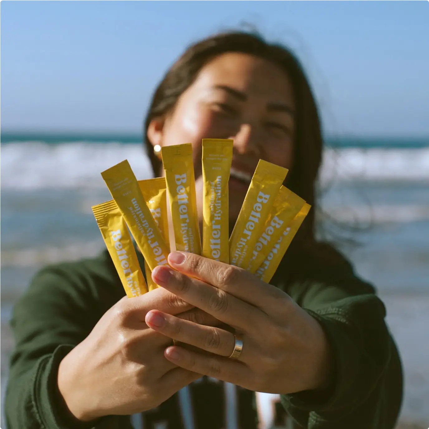 A woman at the beach holds a fan of yellow BetterDays supplement packets