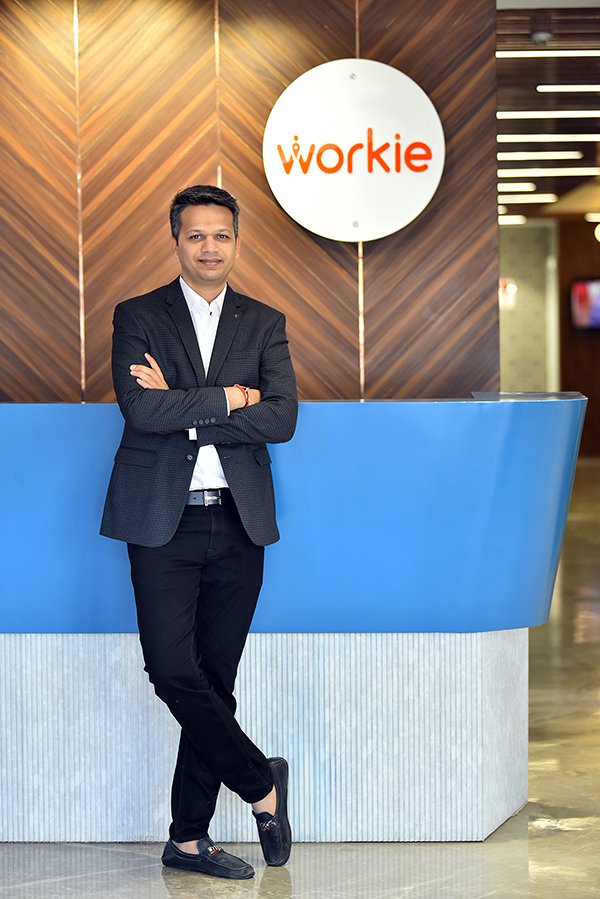 Workie founder Sawan Laddha standing beside a blue reception desk