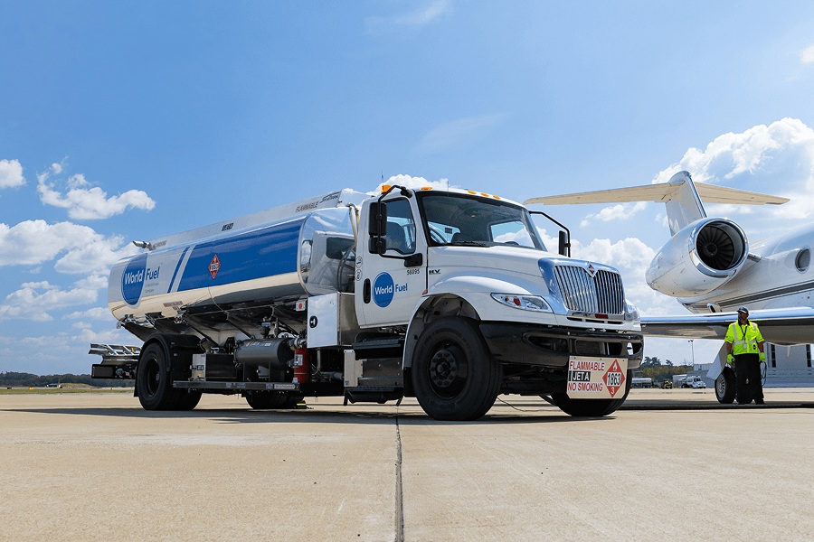 A World Fuel tanker beside a business jet, with a worker standing near the aircraft