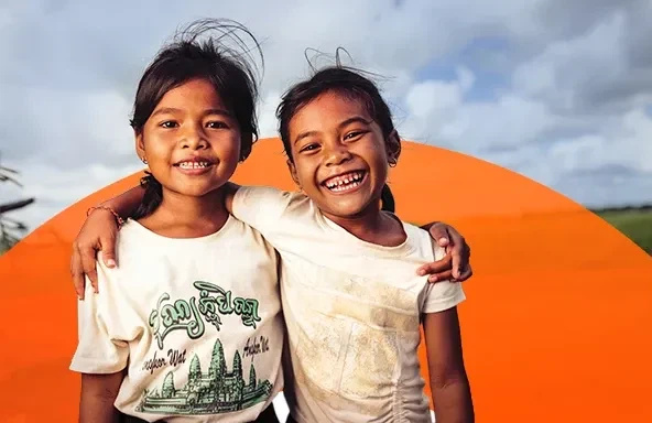 Two girls in Cambodia smile together in a grassy field