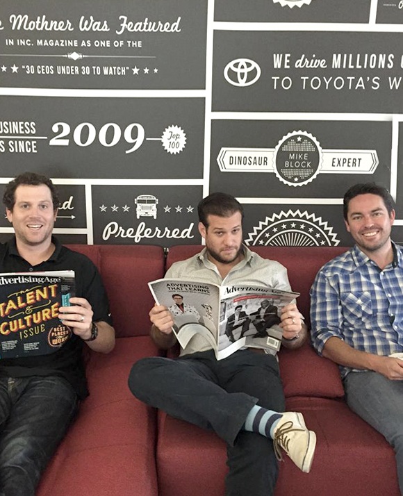 Three early Wpromote leaders seated on a red couch with advertising magazines