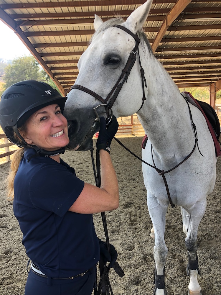 Wynne Ahern smiling beside a saddled white horse under a riding arena roof