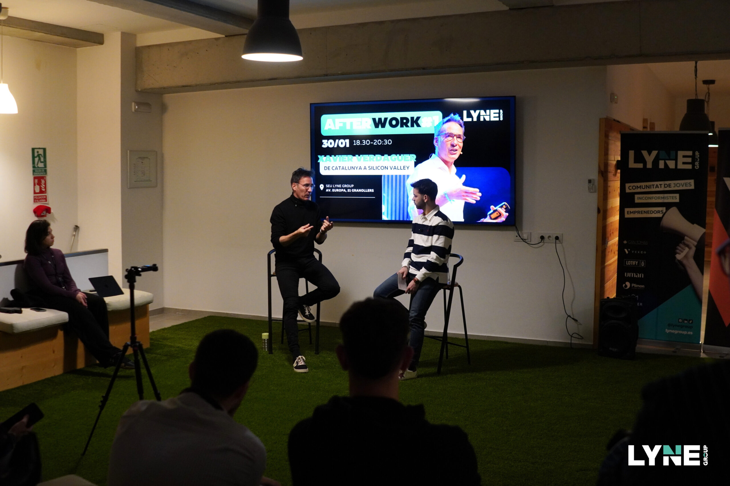 Xavier Verdaguer seated on the left, speaking with an interviewer and an audience at LYNE Group