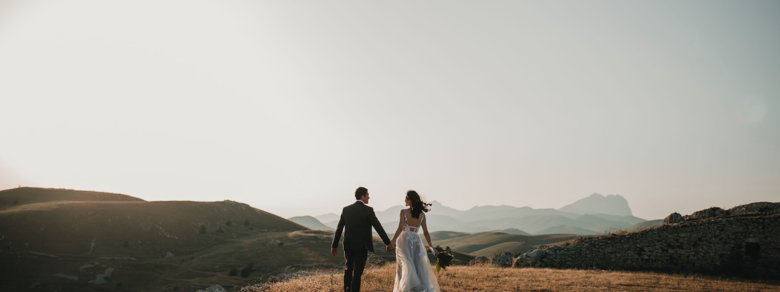 A couple in wedding attire holding hands in an open landscape, from the Stitch and Tie case study