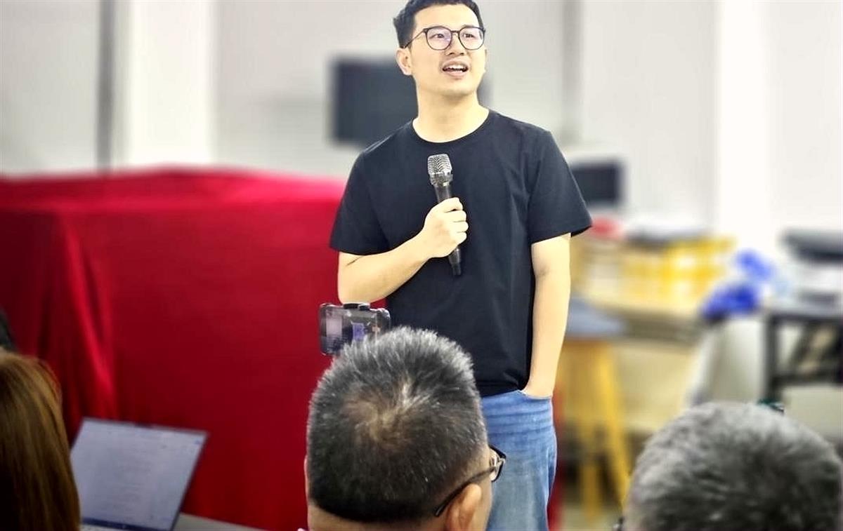 Xiao Hong wearing a black T-shirt and holding a microphone during an entrepreneurship talk