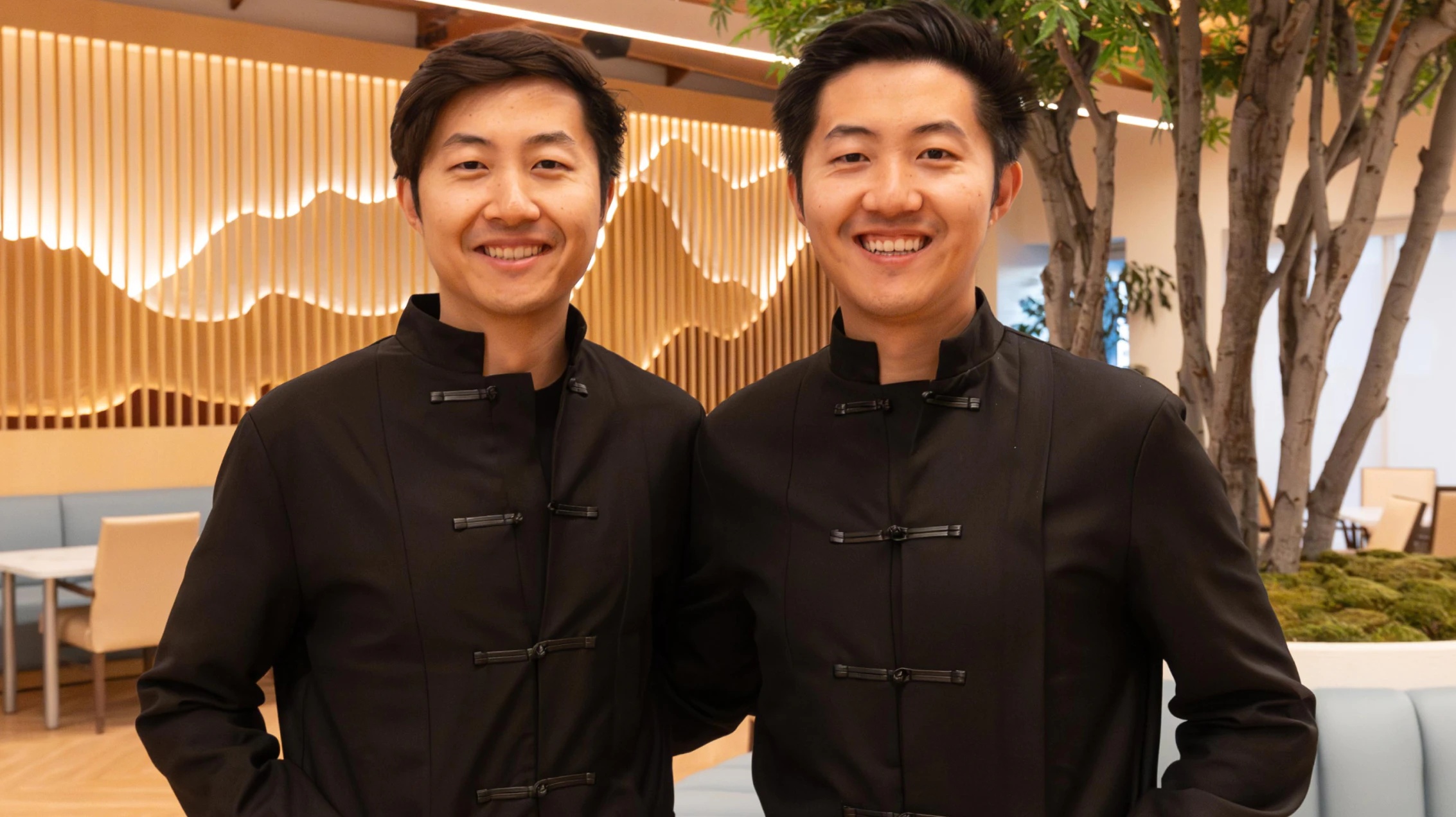 Xing and Yang Su standing together in a wood-lined interior