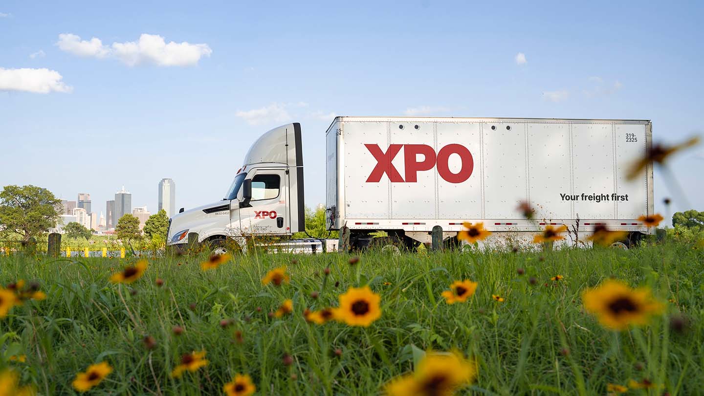 XPO freight truck parked beside a flower field with a city skyline behind it