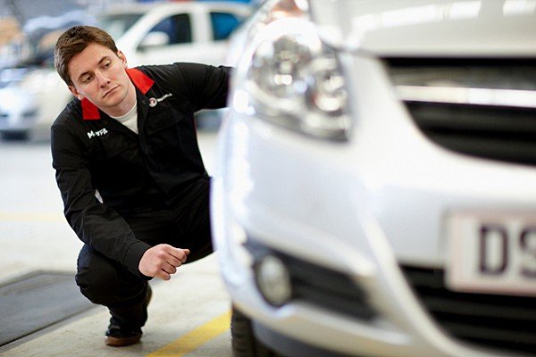 A technician examining the front of a vehicle in a service workshop
