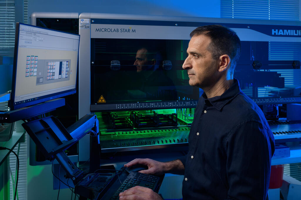 Yanay Ofran working at a computer beside automated laboratory equipment