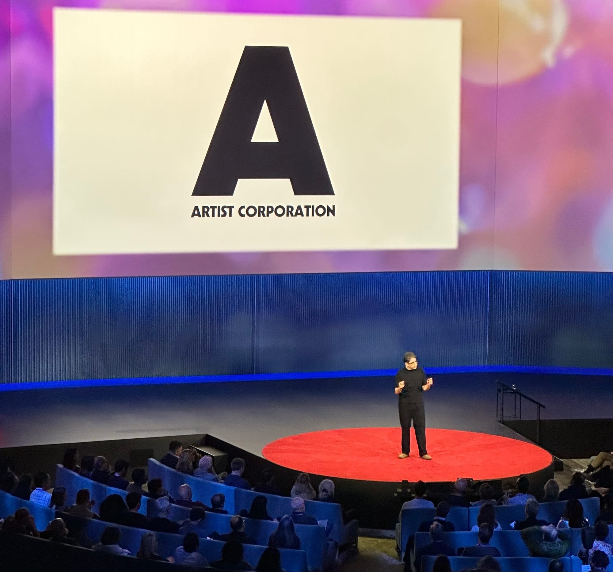 Yancey Strickler on the red TED stage beneath a large Artist Corporation slide