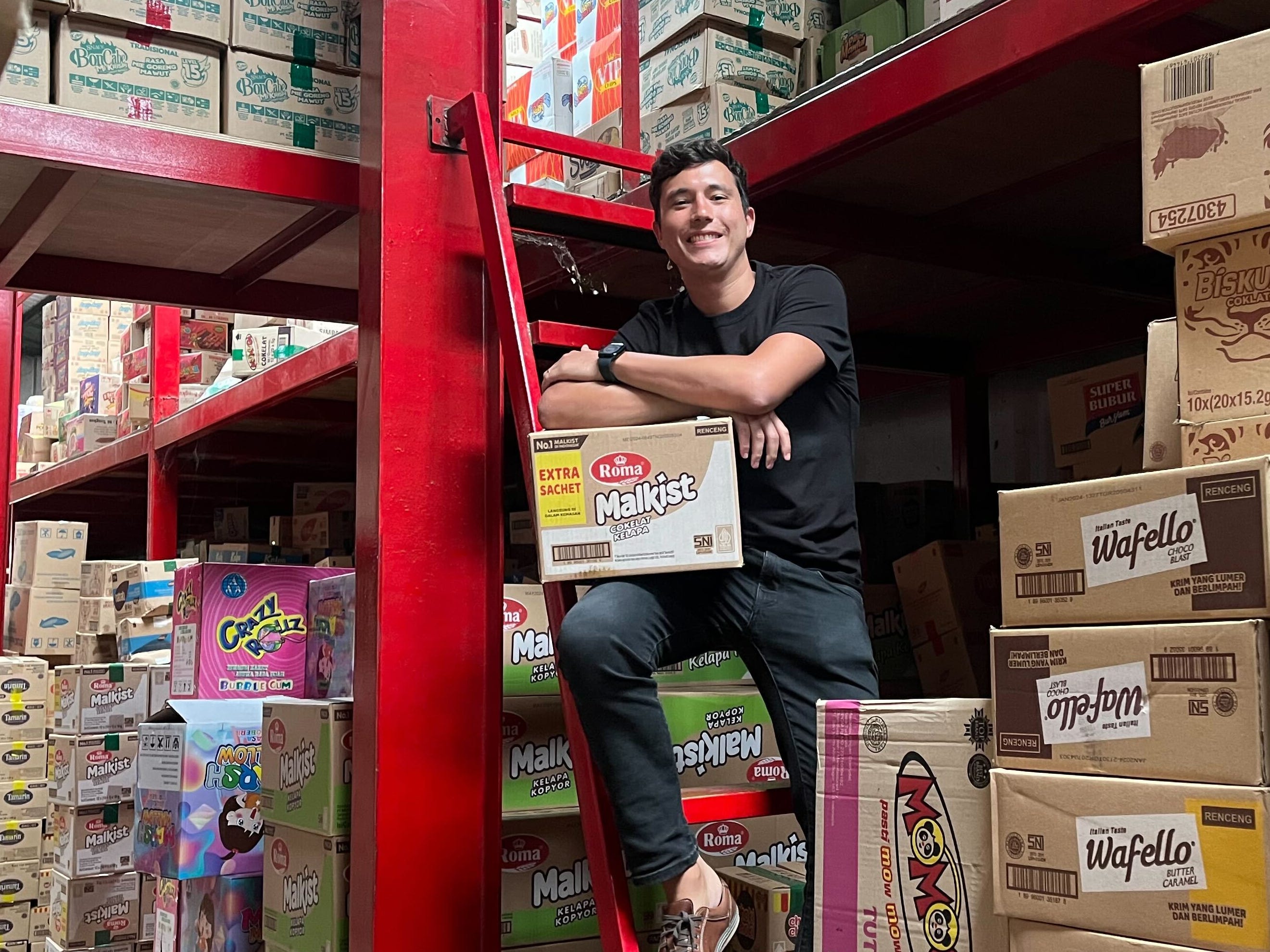 Yann Schuermans sitting among cartons on red warehouse shelving in Jakarta