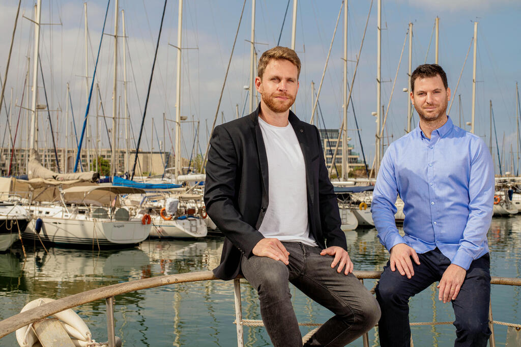 Yarden Gross, left, and Dor Raviv seated beside sailing boats in a marina