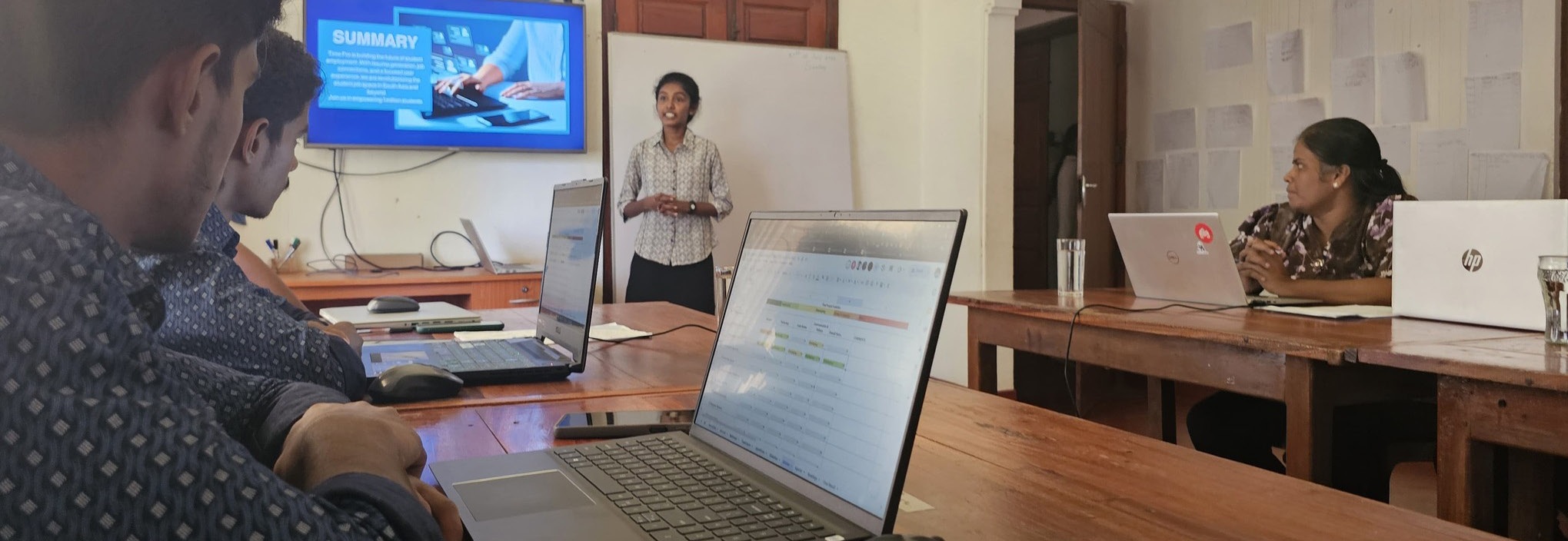 A Uki learner presents to a small classroom with laptops open on the tables
