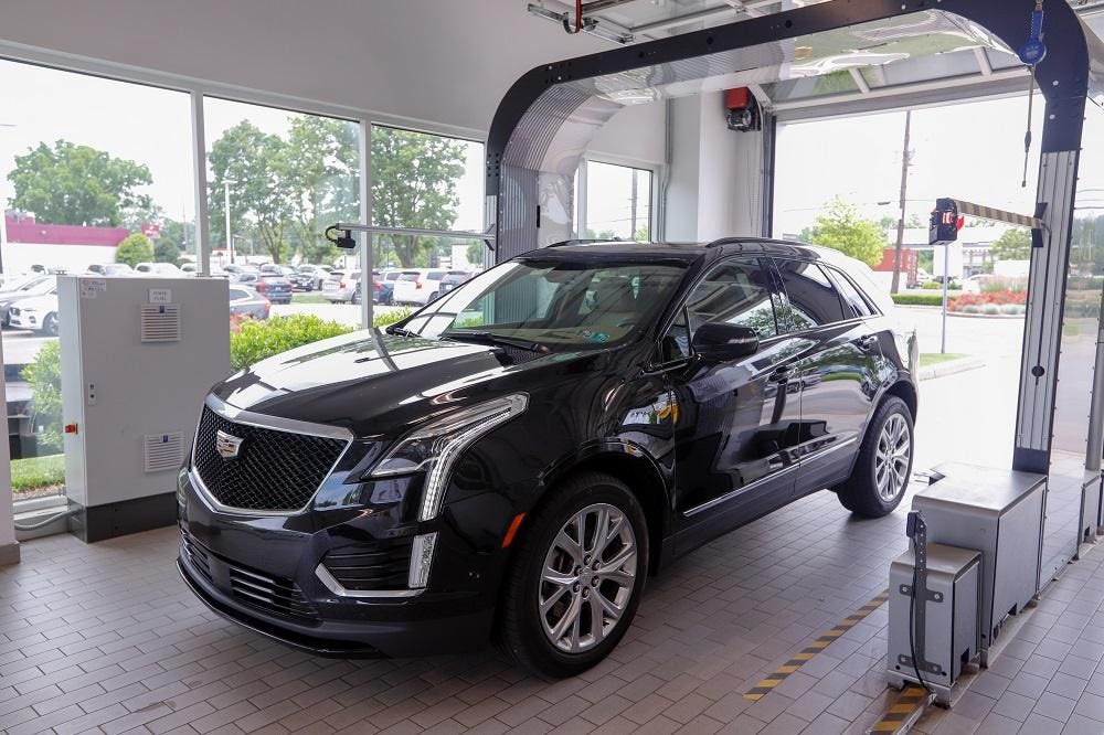 A dark Cadillac SUV passing through a UVeye exterior inspection arch inside a dealership service lane