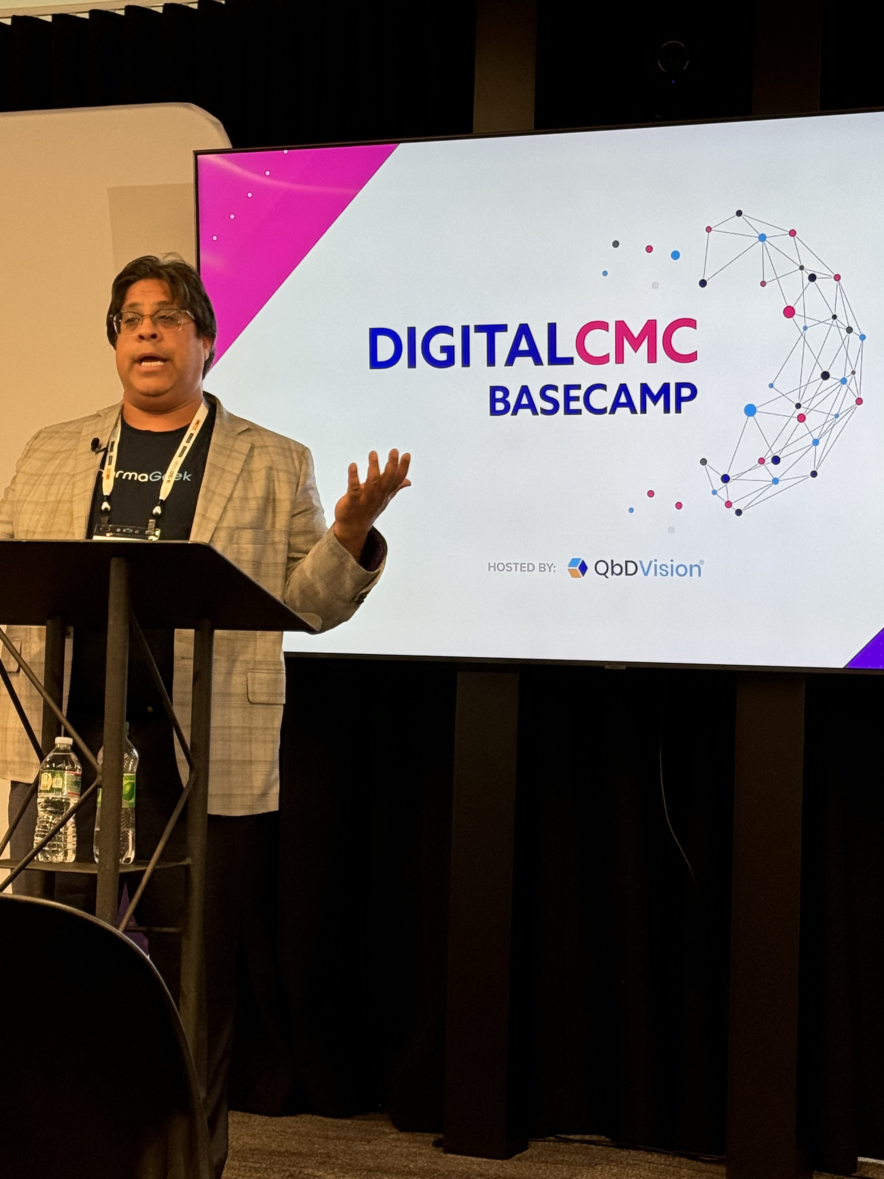 Yash Sabharwal speaking at a lectern beside a Digital CMC Basecamp presentation