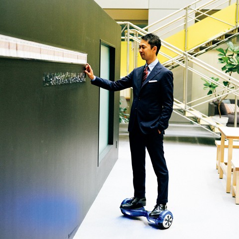 Yasukane Matsumoto in a suit, standing on a self-balancing board inside the RAKSUL office