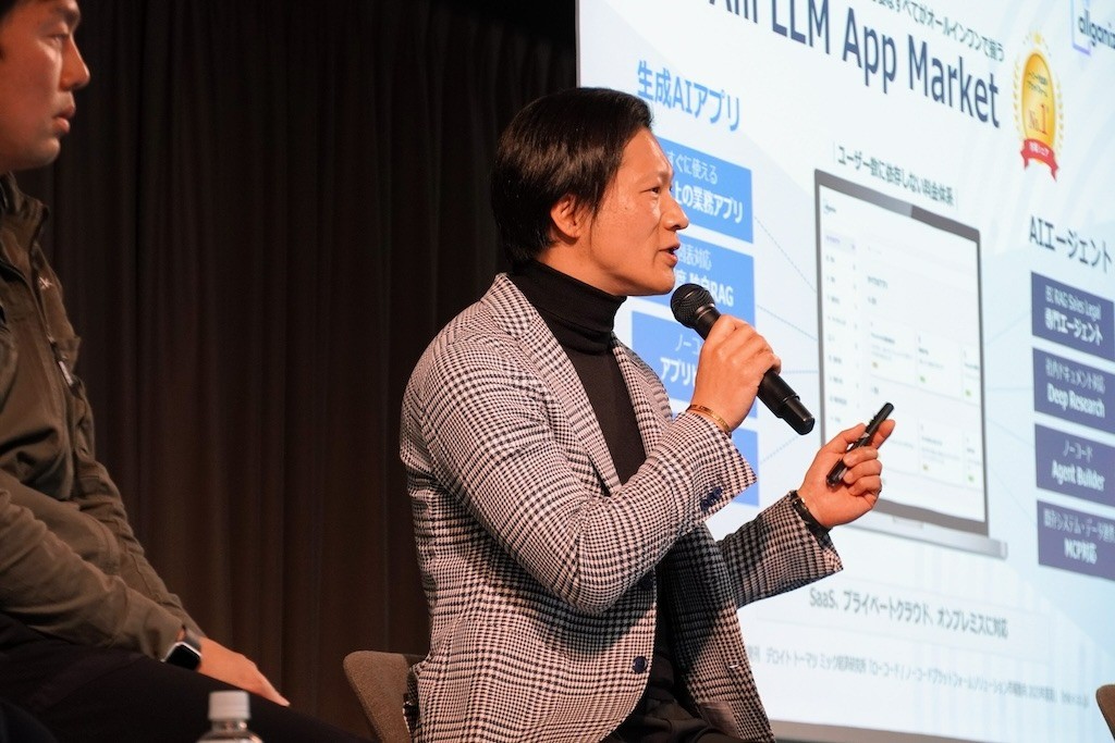 Yasuo Sato holding a microphone and presentation remote during a KDDI Business AI Fes panel