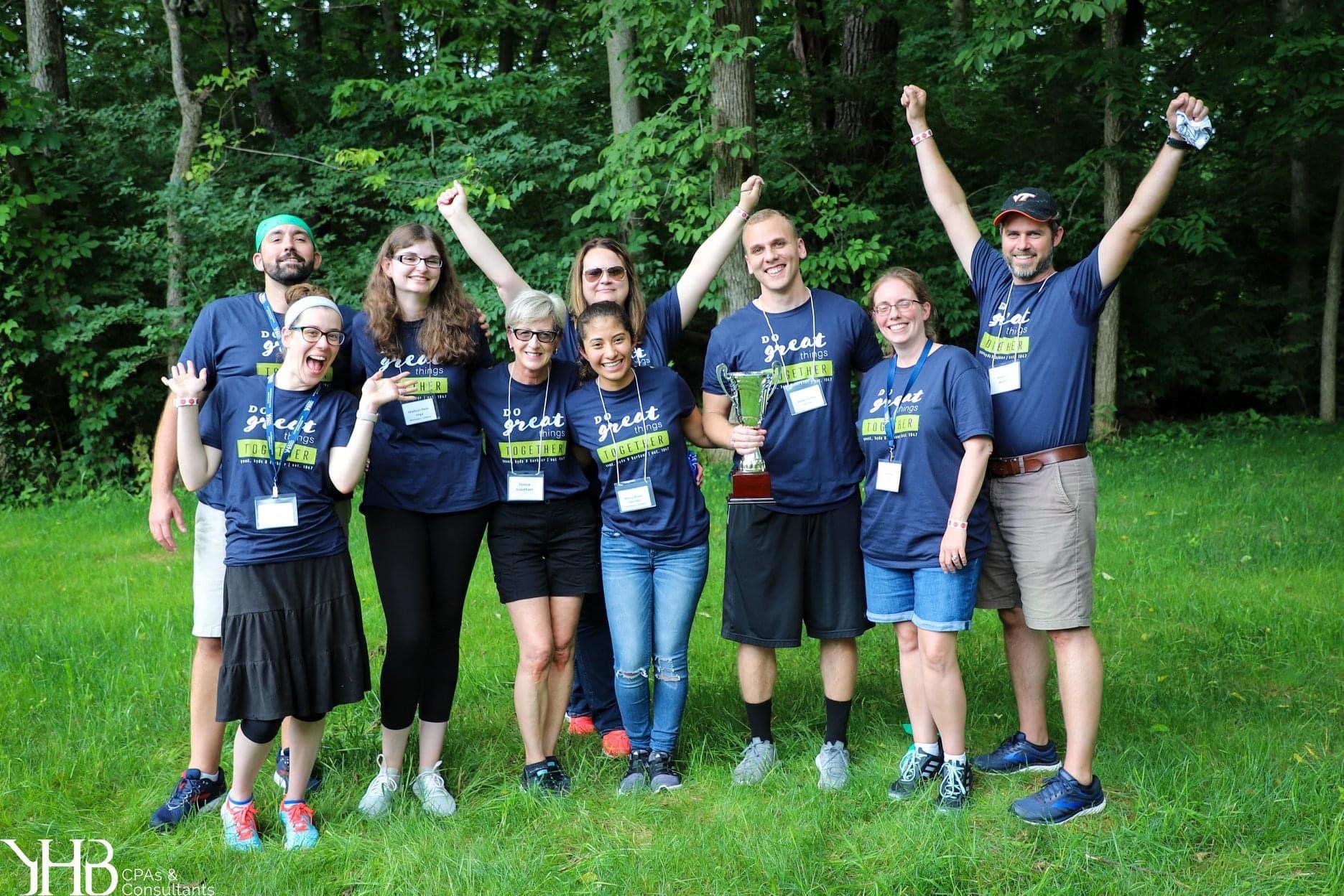 YHB colleagues outdoors in matching navy shirts, gathered around a trophy at Firm Day
