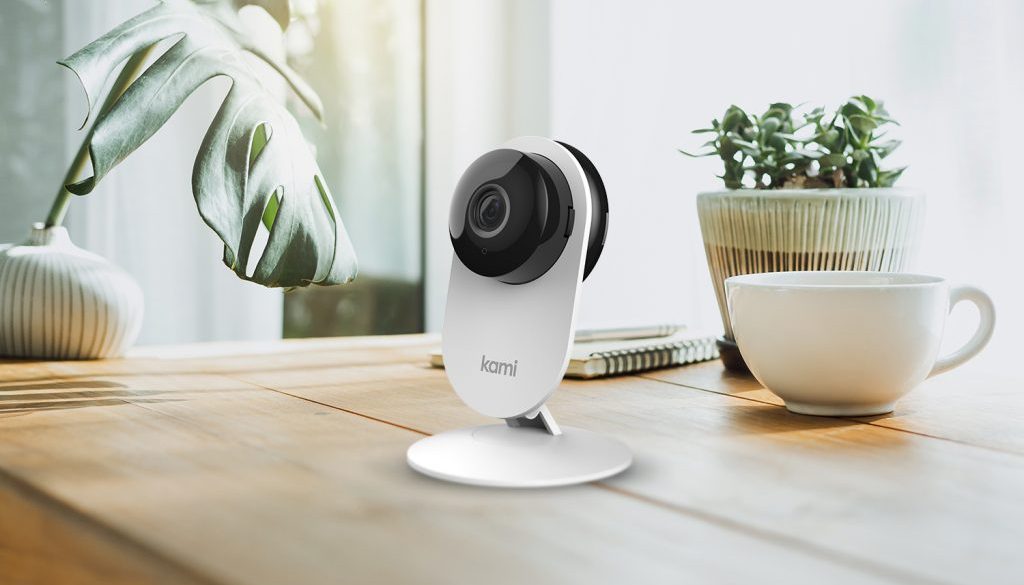 A Kami Mini security camera on a table beside a plant and cup