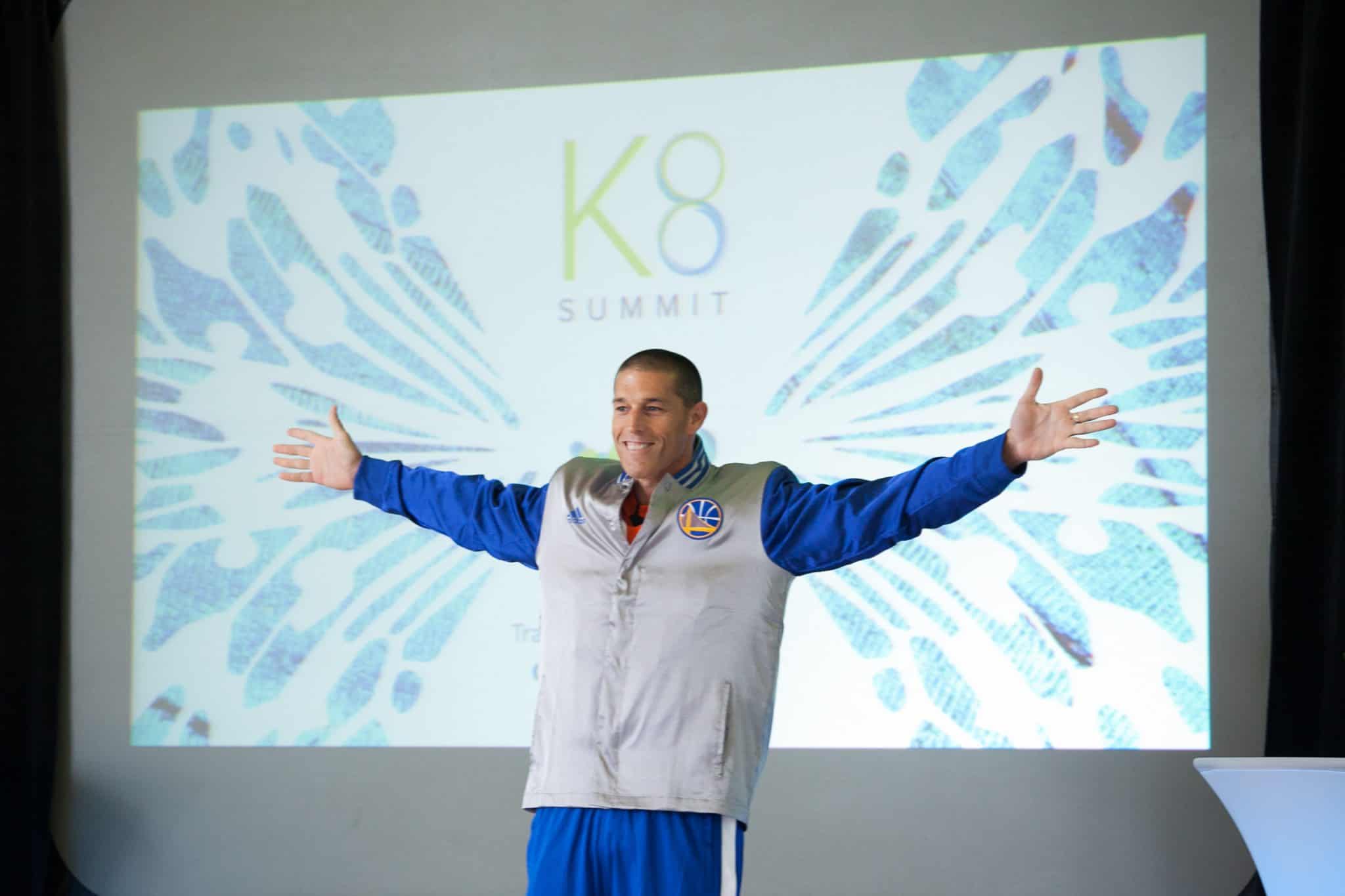 Yoav Izhar-Prato onstage at the 2015 K8 summit, wearing a Warriors jacket with his arms outstretched