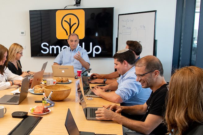 Yonatan Stern speaking with participants around a SmartUp table, with laptops and a whiteboard nearby