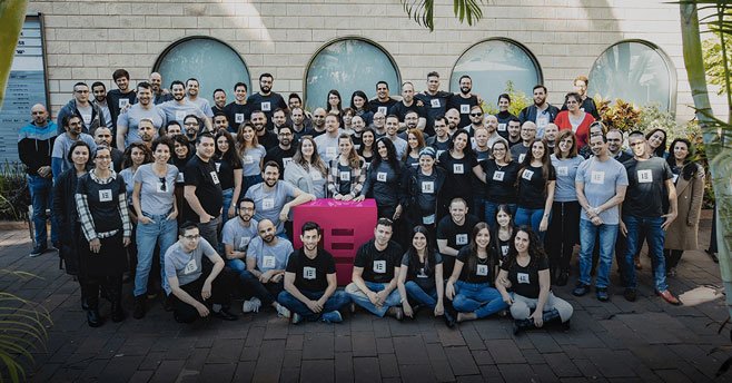 Elementor team members gathered outdoors around a pink Elementor symbol