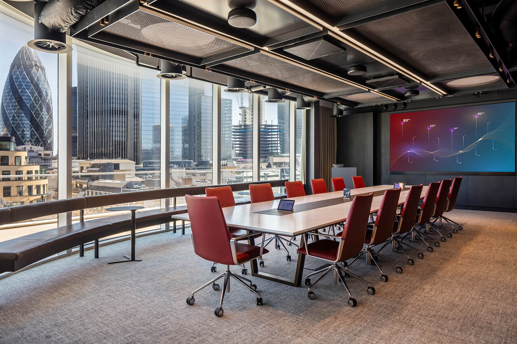 A large meeting room with red chairs, table controllers and a wall display overlooking London
