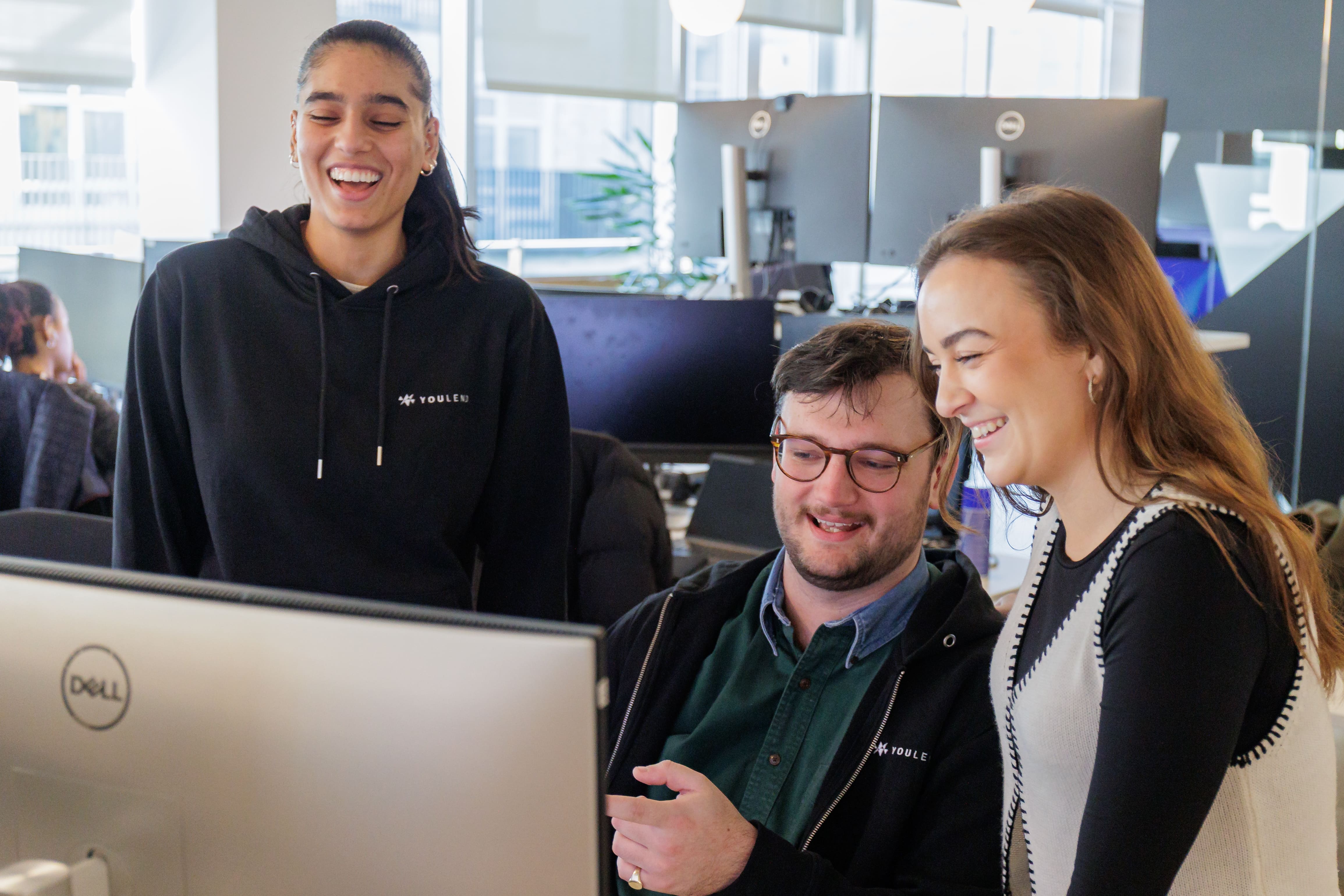 Three YouLend colleagues gathered around a computer in a bright office